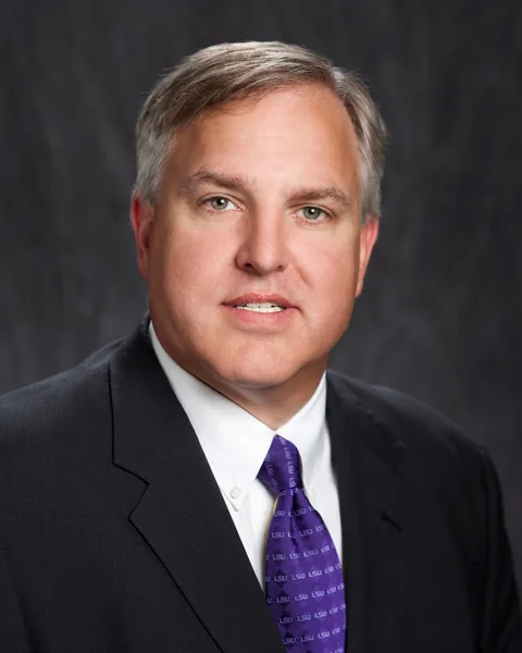 Ray Castle wearing a black suit, white shirt, and a purple tie.
